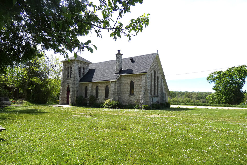 St. Margaret’s Chapel in Cape Chin, Ontario – a small limestone church with red-trimmed gothic windows surrounded by trees and open lawn.
